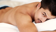 Homem deitado na cama, se vendo somente o rosto e o tronco, com um ar leve pensando sobre o que é fio terra e como fazer.